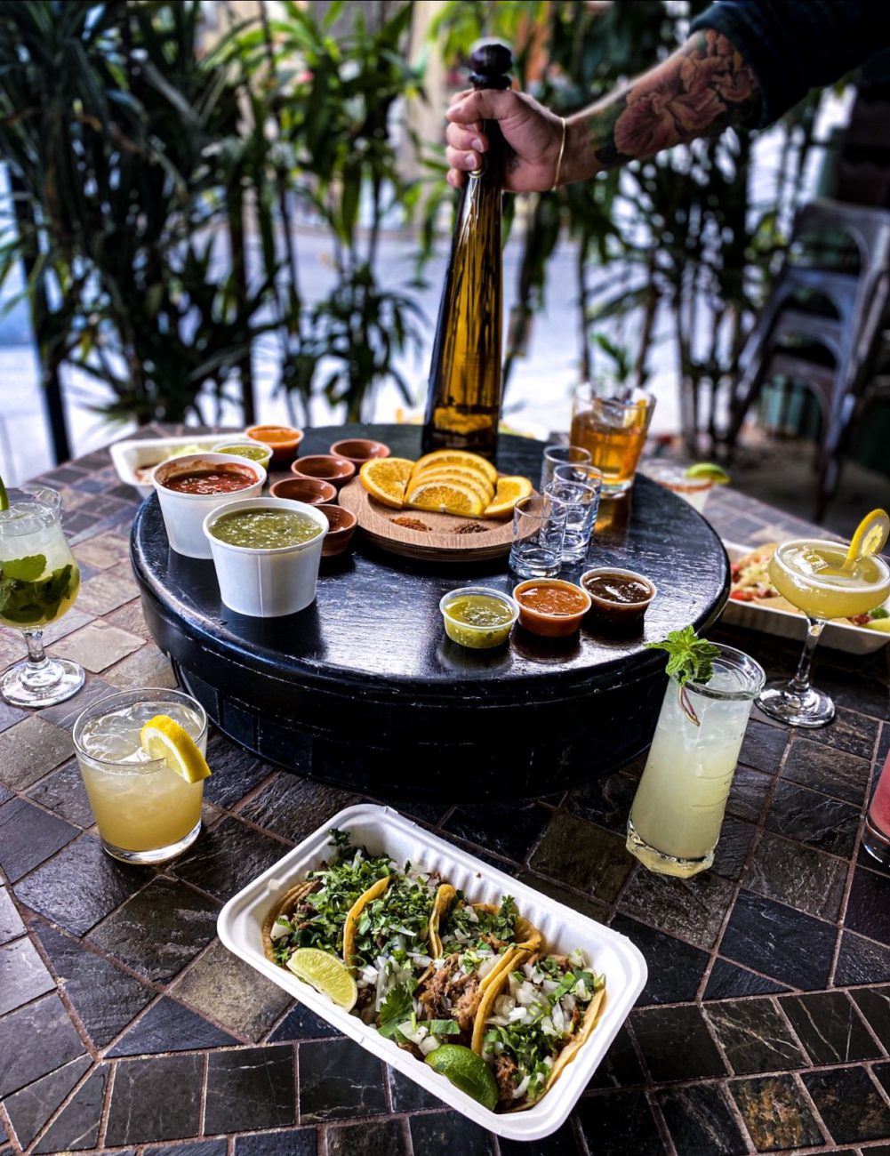 Tequila bottle and salsa flight on a lazy susan with margaritas, mojito, and street tacos at El Pueblo's bar