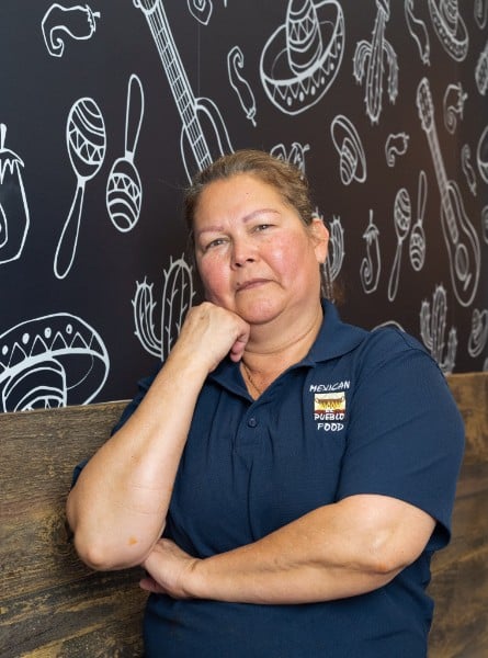 El Pueblo team member resting against a wooden bar in front of the signature Mexican-icon mural