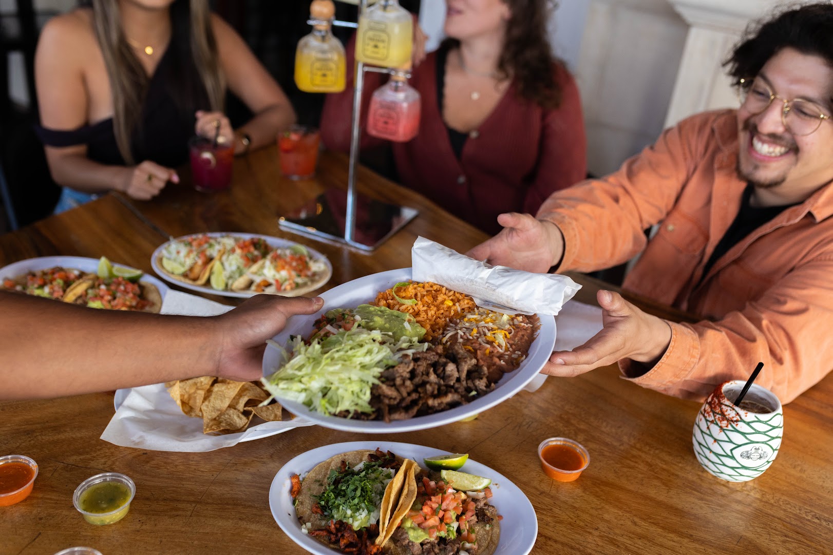 A carne asada plate being passed across the table with rice, beans, guacamole, and chips at El Pueblo