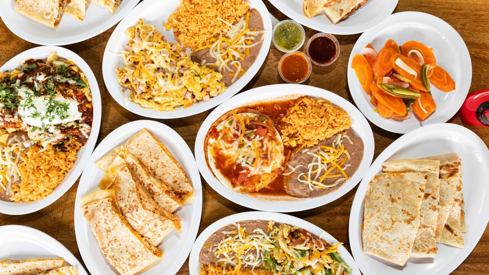 An overhead spread of El Pueblo plates — chilaquiles, huevos rancheros, quesadillas, rice, beans, and salsas