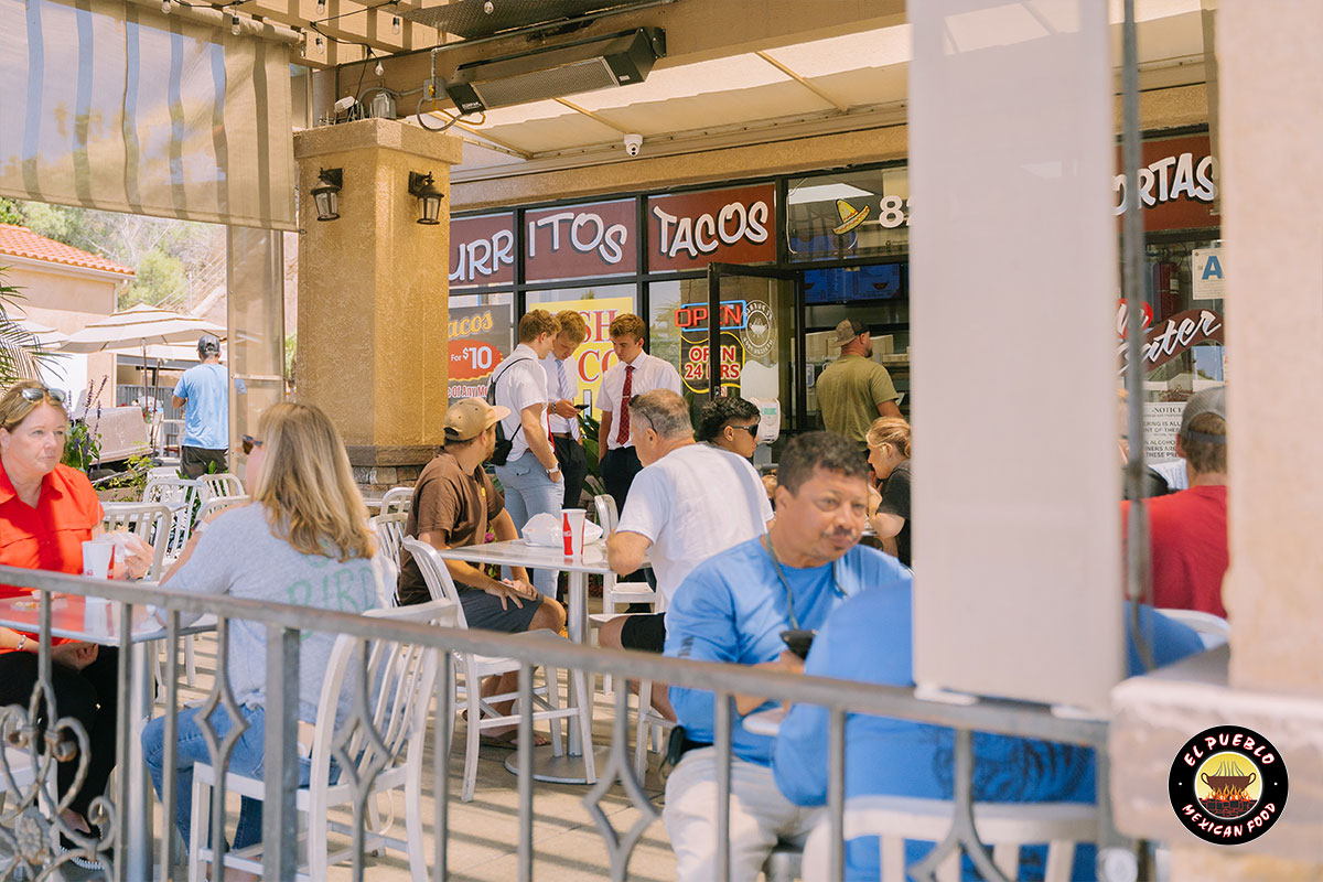 A busy El Pueblo patio scene — guests dining outside under the burritos and tacos signage